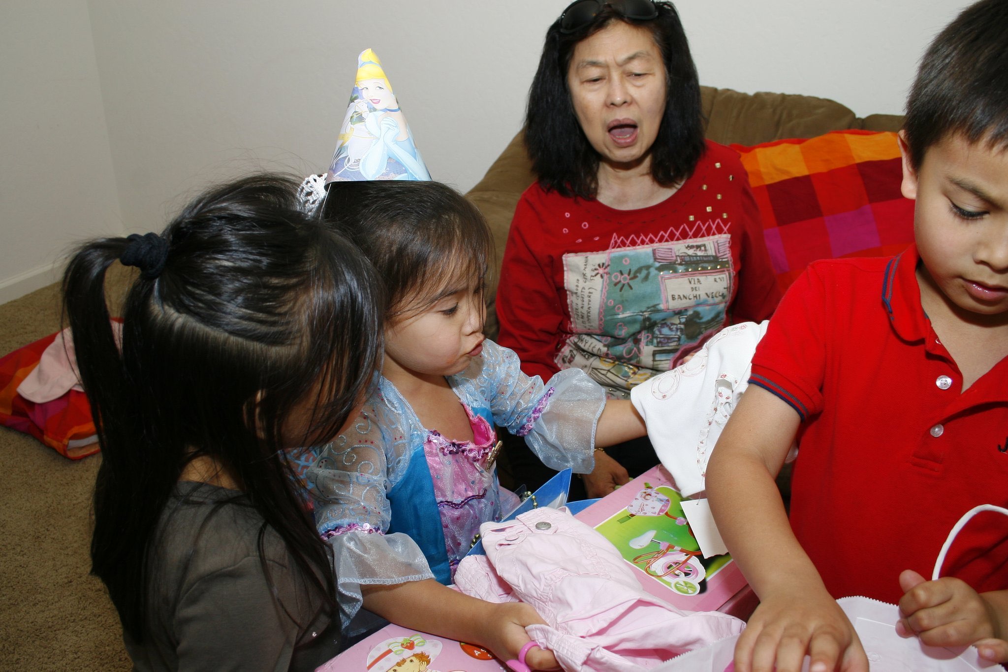 Children opening birthday gifts while family watches nearby