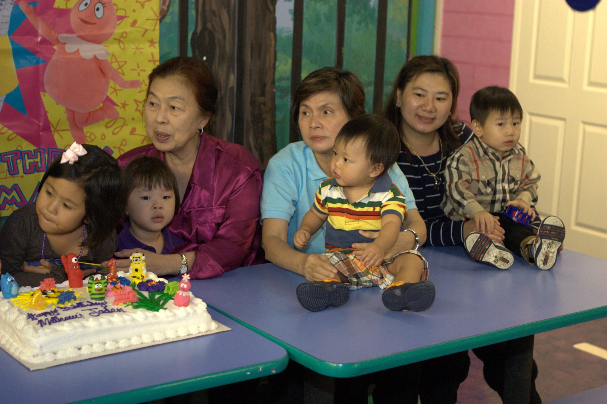 Family gathered around a first birthday cake at a children's table