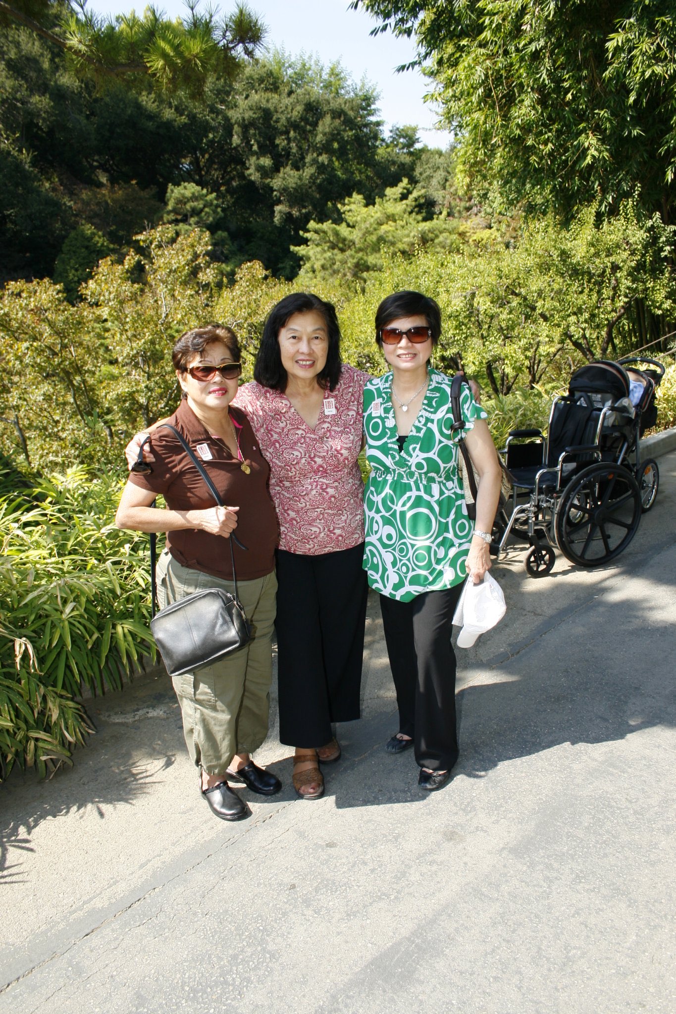 Three women standing arm-in-arm on a garden pathway