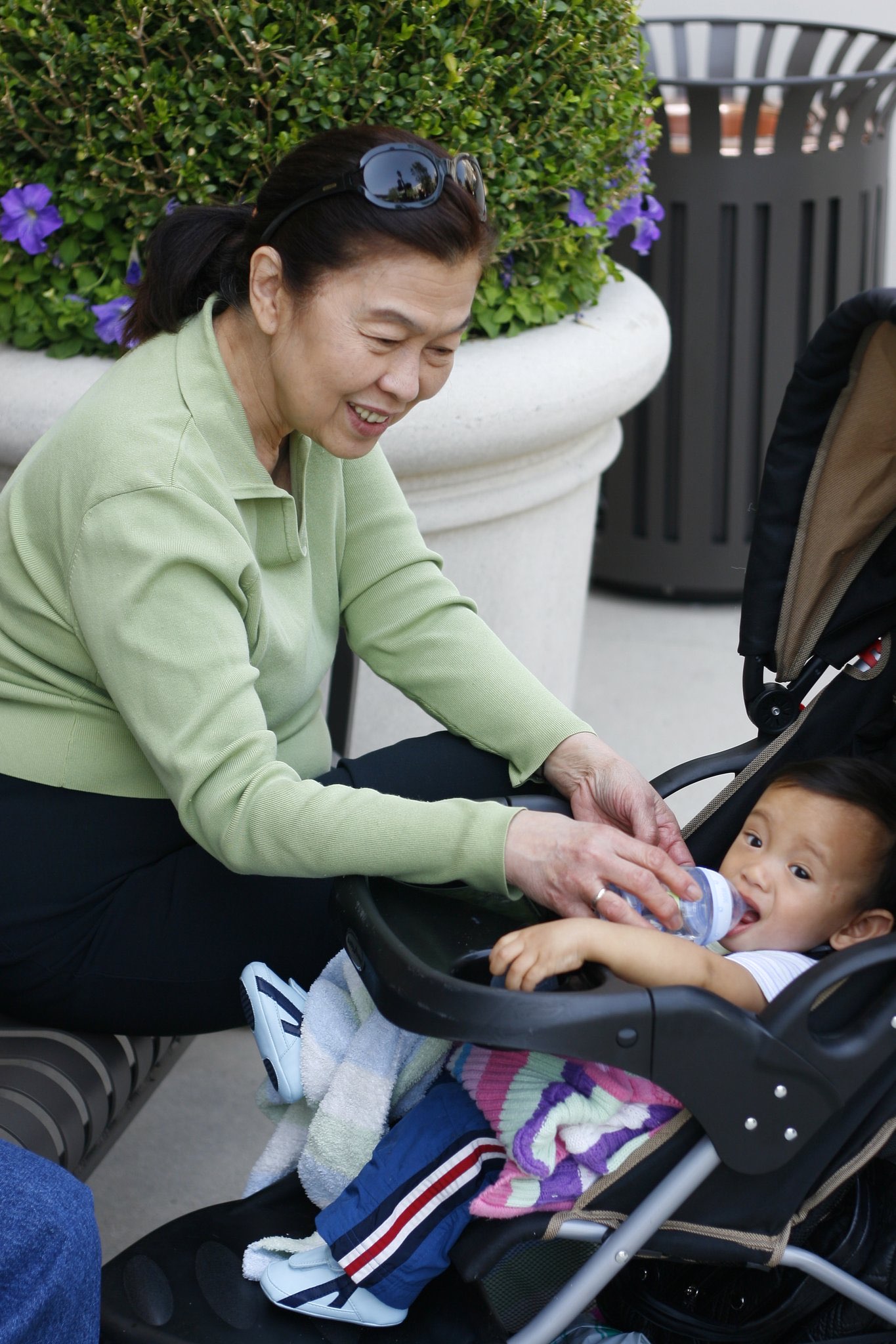 An older woman helping a toddler drink from a bottle outdoors