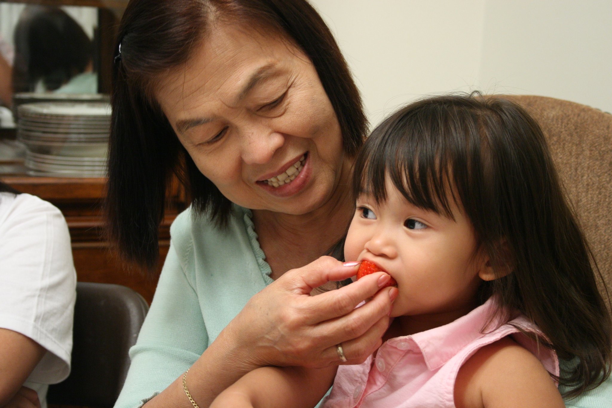An older woman offering a strawberry to a young child indoors