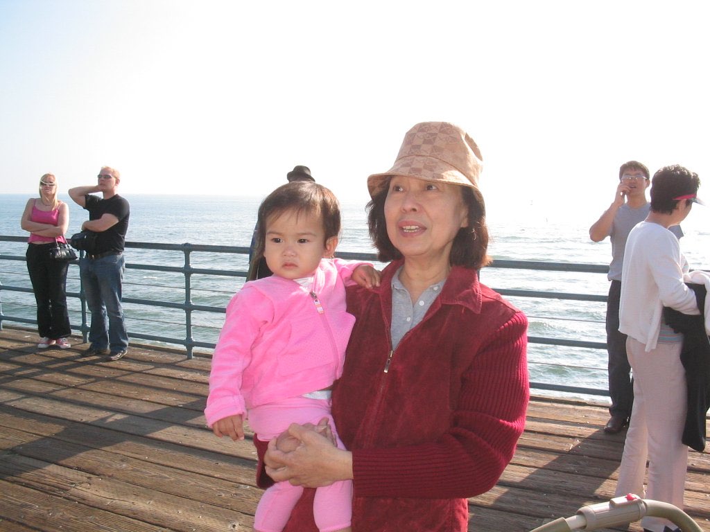 An older woman holding a toddler on a pier by the ocean