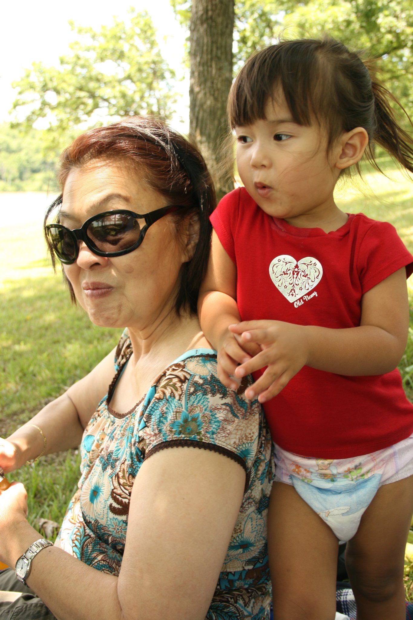 An older woman sitting outdoors beside a young toddler on a sunny day